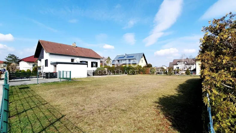 Großes unbebautes Grundstück mit Rasenfläche und umliegenden Wohnhäusern unter blauem Himmel.