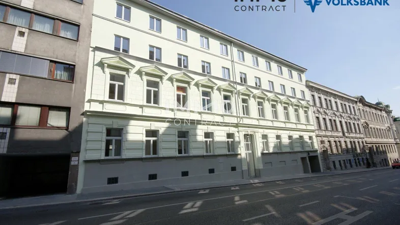 Fassade eines Mehrfamilienhauses an einer Stadtstraße mit klassischer Architektur und vielen Fenstern.