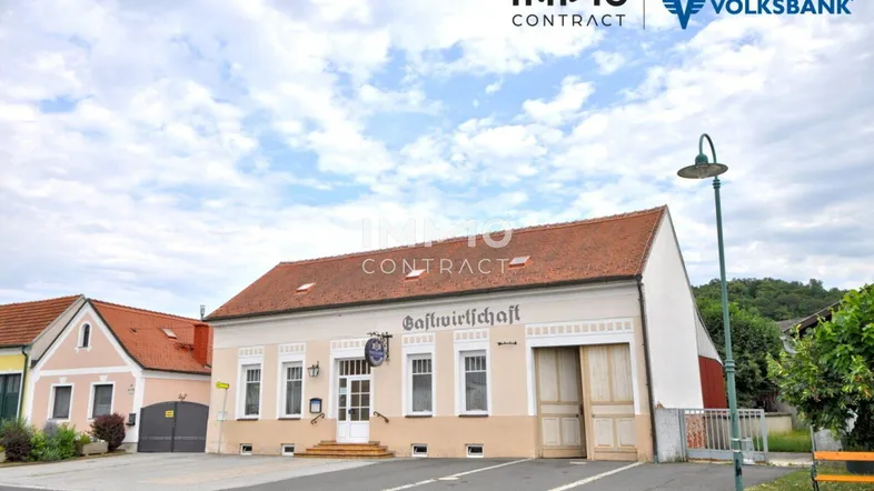 Traditionelles Gasthaus mit Ziegeldach und hell gestrichener Fassade unter bewölktem Himmel.
