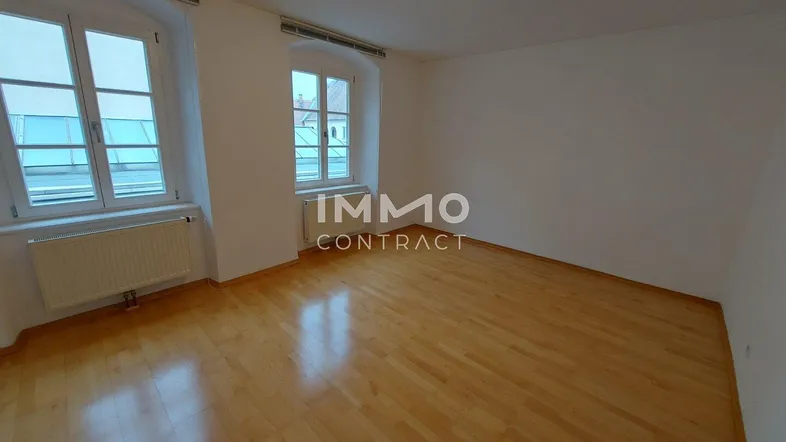 Helles Zimmer mit Parkettboden und zwei Fenstern, bereit zur individuellen Gestaltung.