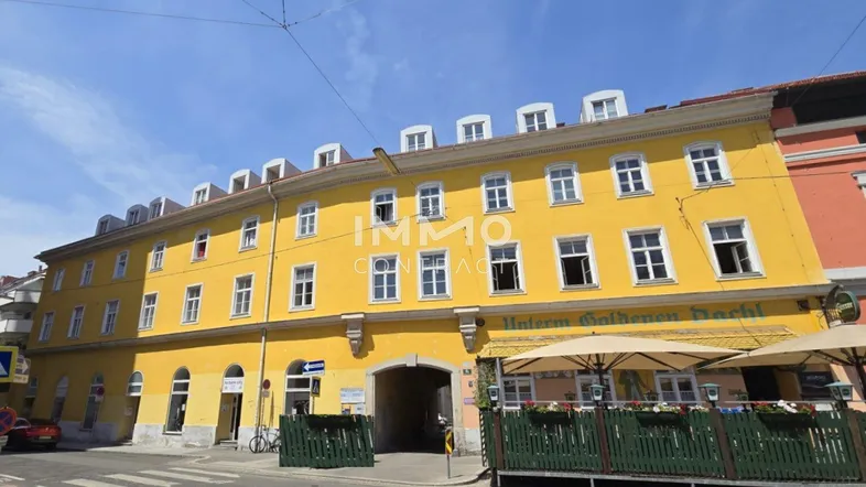 Gelbes Gebäude mit vielen Fenstern, einem Torbogen und einem Restaurant mit Außenterrasse.