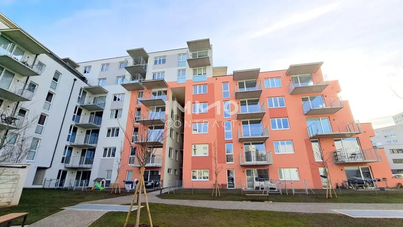 Modernes Mehrfamilienhaus mit farbiger Fassade und zahlreichen Balkonen, umgeben von einer Grünfläche.