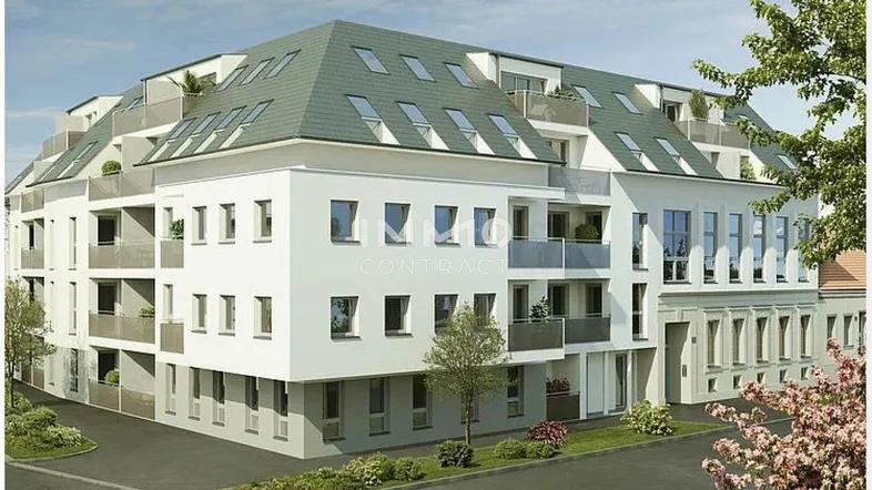 Moderne Wohnanlage mit weißer Fassade, Balkonen und Mansarddach in städtischer Umgebung.