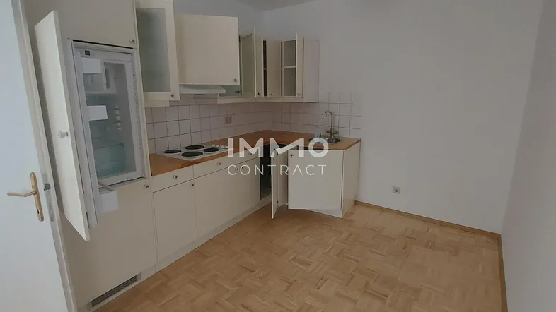 Funktionale Küche mit weißen Schränken, integriertem Kühlschrank und Kochfeld, sowie Parkettboden.
