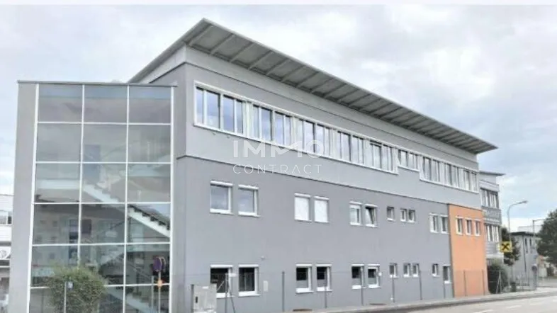 Modernes Geschäftsgebäude mit grauer Fassade, großen Fenstern und einem verglasten Treppenhaus.