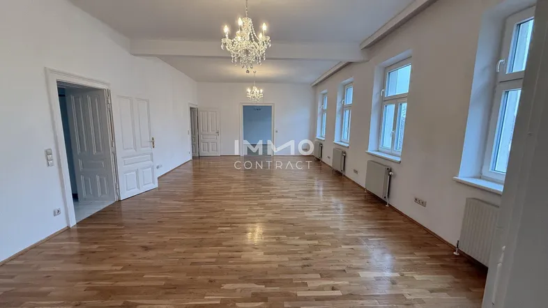 Geräumiges, helles Zimmer mit Parkettboden und hohen Fenstern, ideal als Wohnbereich.
