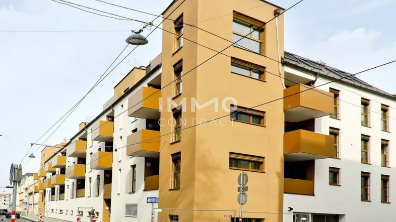Modernes Mehrfamilienhaus mit gelber Fassade und Balkonen an einer städtischen Straße.