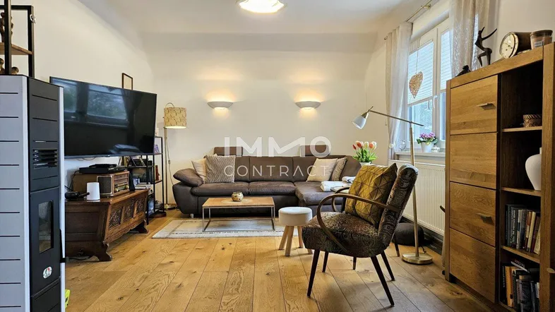 Gemütliches Wohnzimmer mit Holzboden, großem Sofa und einem modernen Kaminofen.