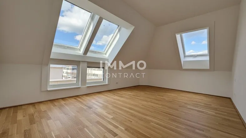 Helles Dachzimmer mit Holzboden und mehreren Dachfenstern, das viel Tageslicht hereinlässt.