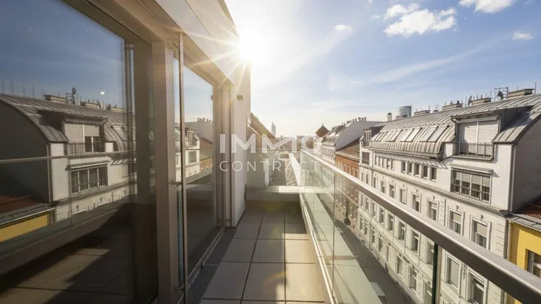 Geräumiger Balkon mit Glasgeländer und weitem Blick über die Dächer der Stadt bei Sonnenuntergang.
