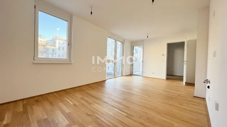 Heller Wohnbereich mit Parkettboden, großen Fenstern und Zugang zum Balkon.