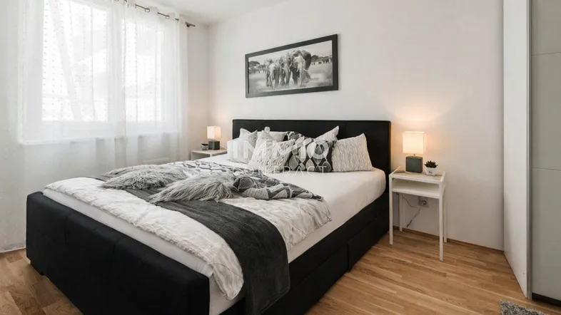 Helles Schlafzimmer mit großem Doppelbett, Parkettboden und Fenster mit Vorhängen.