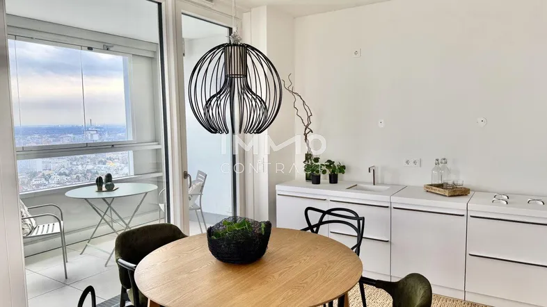Moderner Essbereich mit Holztisch, minimalistischer Küchenzeile und Zugang zu einem Balkon mit Stadtblick.