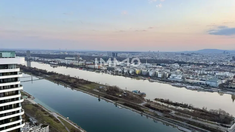 Panoramablick über die Stadt und den Fluss bei Sonnenuntergang, mit modernen Gebäuden am Ufer.