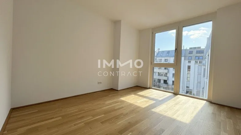 Heller Raum mit Parkettboden und großen Fenstern, die viel Tageslicht hereinlassen.