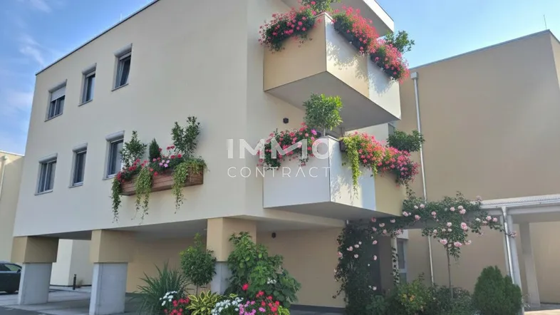 Modernes Gebäude mit mehreren Balkonen, die mit bunten Blumenkästen geschmückt sind.