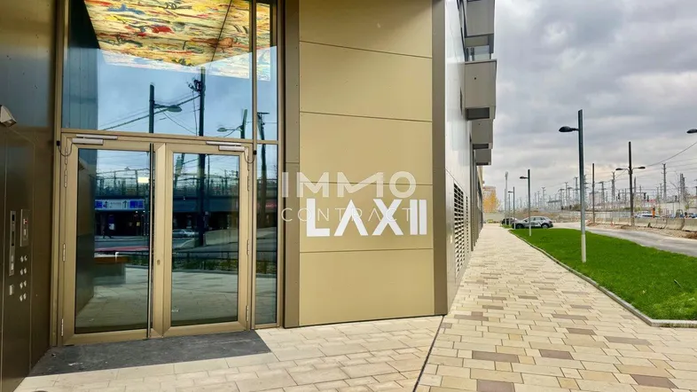 Moderner Gebäudeeingang mit großen Glasfronten und gepflastertem Gehweg in urbaner Umgebung.