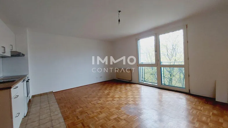 Heller Wohnbereich mit Parkettboden, großen Fenstern und integrierter Küchenzeile.