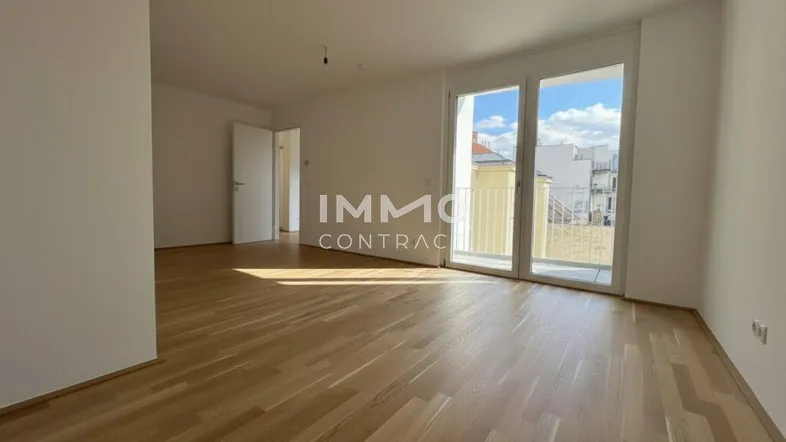 Heller, leerer Wohnraum mit Parkettboden und großen Fenstern, die Zugang zu einem Balkon bieten.