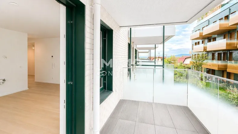 Geräumiger Balkon mit Fliesenboden, Glasbrüstung und Blick auf die Umgebung.