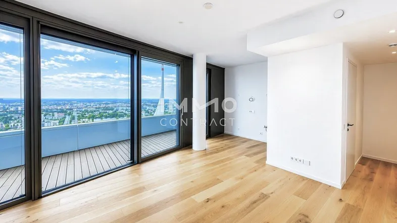 Geräumiger Wohnbereich mit hellem Holzboden und großen Fenstern, die viel Tageslicht hereinlassen.