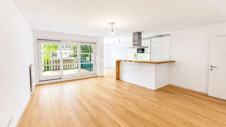 Heller offener Wohnbereich mit Parkettboden, moderner Küche und Zugang zum Balkon.