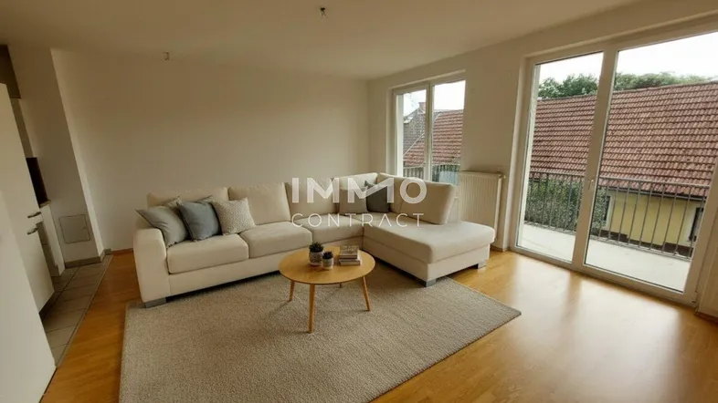 Helles Wohnzimmer mit beigem Ecksofa, Holzboden und Zugang zu einem Balkon.