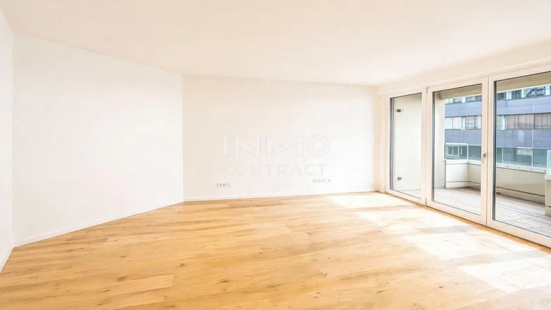 Helles, leeres Zimmer mit neuem Parkettboden und großen Fenstern zum Balkon.