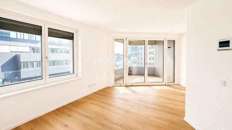 Helles, leeres Wohnzimmer mit Parkettboden und Zugang zu einem Balkon, bietet viel natürliches Licht.