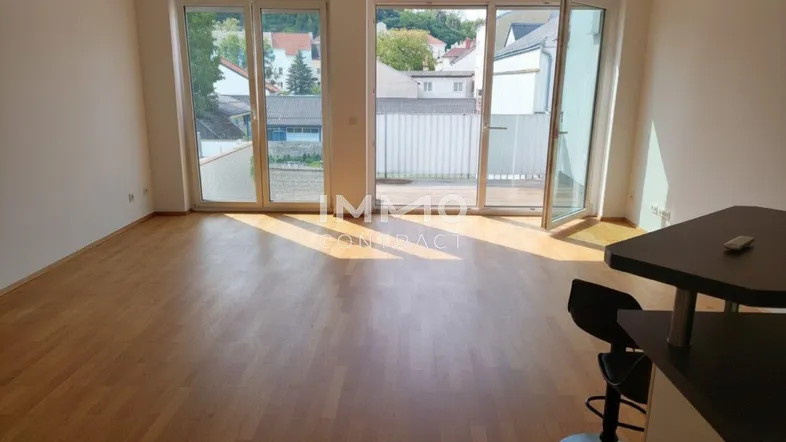 Helles Wohnzimmer mit Parkettboden und Zugang zu einem Balkon, der viel Tageslicht hereinlässt.