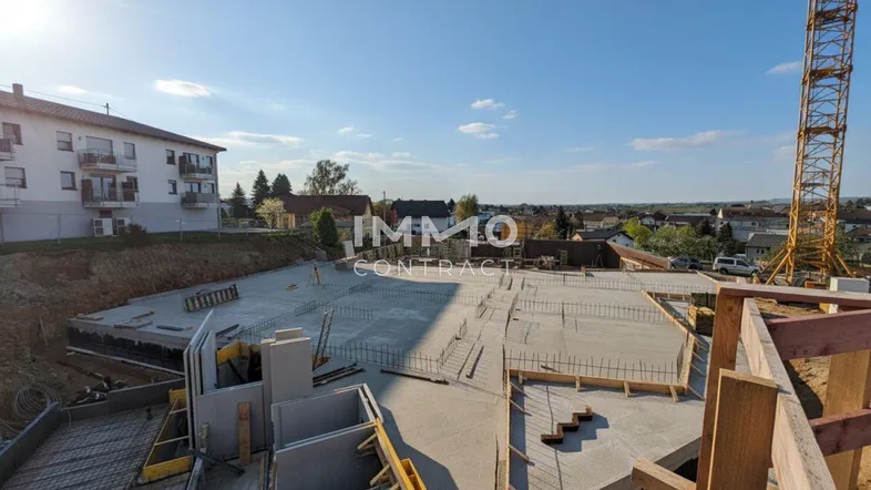 Baustelle mit bereits gegossener Bodenplatte und vorbereiteter Bewehrung für den weiteren Baufortschritt unter blauem Himmel.