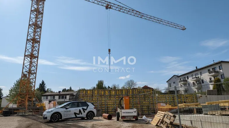 Baustelle mit großem Kran und im Bau befindlichem Gebäude unter blauem Himmel an einem sonnigen Tag.