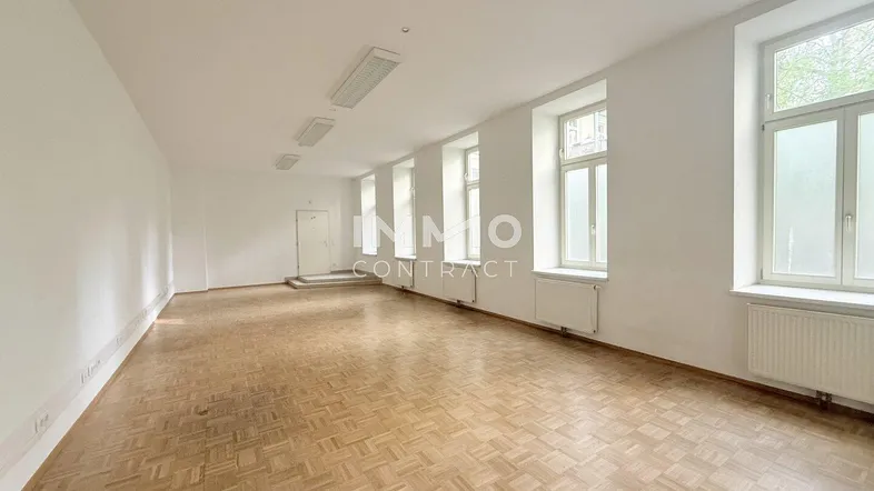 Großer, leerer Raum mit Fischgrätparkett und mehreren Fenstern, ideal für Büronutzung oder flexible Gestaltung.