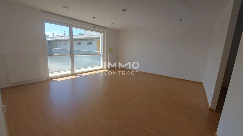 Helles Wohnzimmer mit Laminatboden und großem Fenster mit Zugang zu einem Außenbereich.