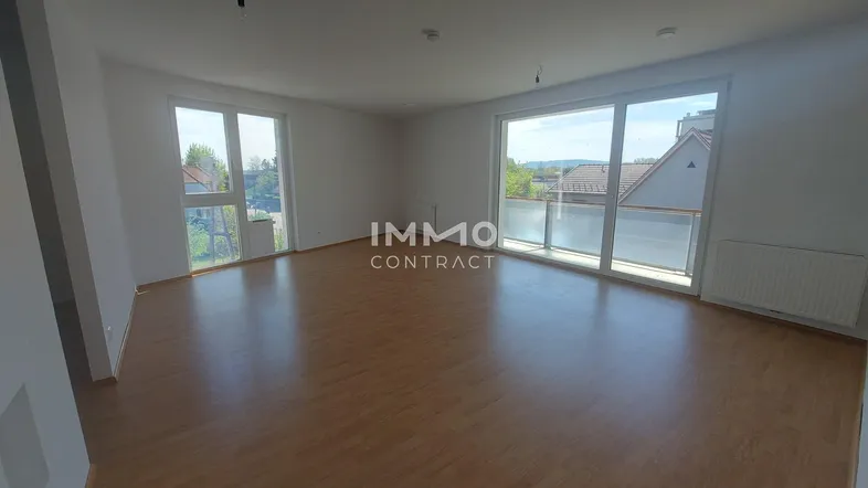 Heller Wohnraum mit großen Fenstern, Laminatboden und Zugang zum Balkon.