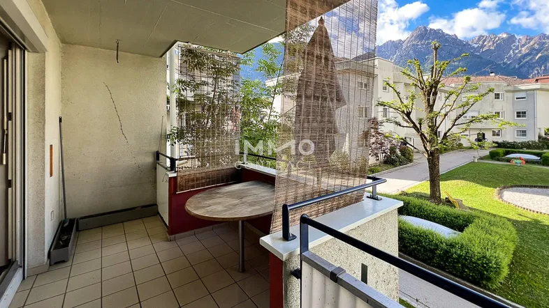 Balkon mit Holztisch, Fliesenboden und schöner Aussicht auf die Berge und den Gemeinschaftsgarten.