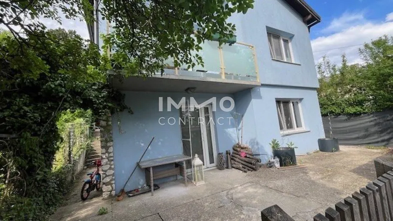 Ansicht der blauen Hausfassade mit kleinem Balkon und gepflastertem Bereich neben dem Gebäude.