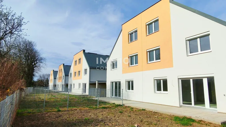Reihe moderner Neubauten mit hellen Fassaden und großen Fenstern unter blauem Himmel.