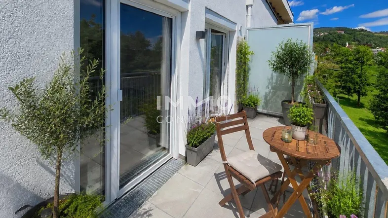 Heller Balkon mit Sitzgelegenheiten, Pflanzen und weitem Blick ins Grüne.