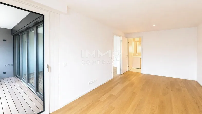 Helles, leeres Wohnzimmer mit Holzboden und Zugang zu einem Balkon, der viel Tageslicht hereinlässt.