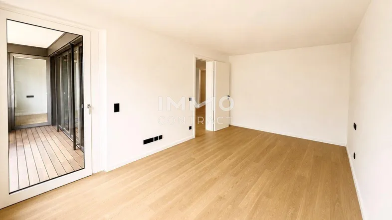 Helles Zimmer mit Holzboden und Zugang zu einem Balkon, ideal als Wohn- oder Schlafbereich.
