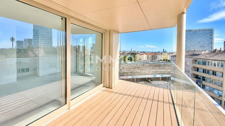 Geräumiger Balkon mit Holzboden und Glasgeländer, bietet einen weiten Blick über die Stadt.