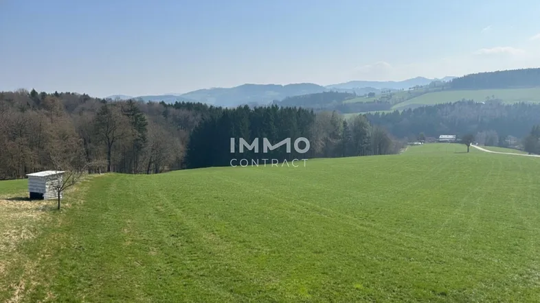 Panoramablick über weite grüne Felder und Wälder mit hügeliger Landschaft im Hintergrund bei klarem Wetter.