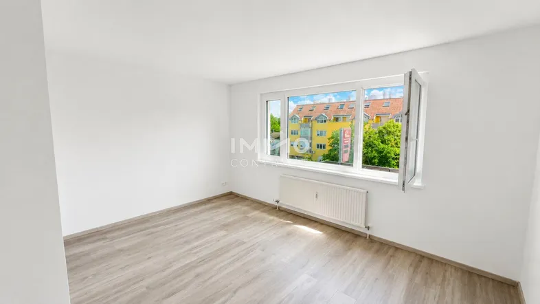 Helles Zimmer mit Laminatboden und Blick auf die umliegenden Gebäude und Bäume.