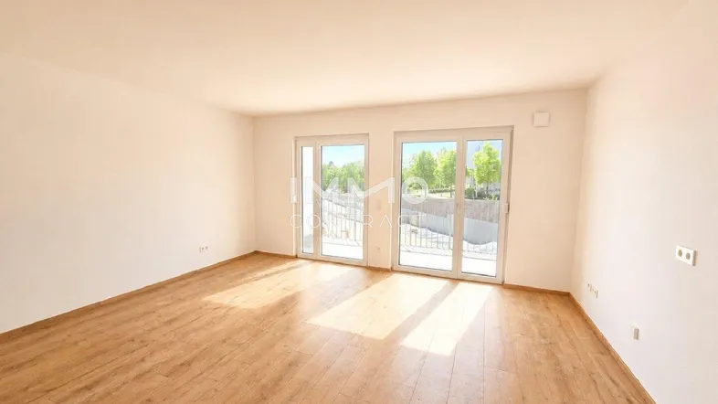 Helles, leeres Zimmer mit Holzboden und Zugang zu einem Außenbereich, ideal als Wohnzimmer.