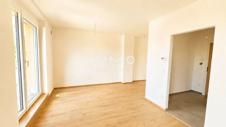 Helles, leeres Zimmer mit modernem Laminatboden und Zugang zu einem Außenbereich.