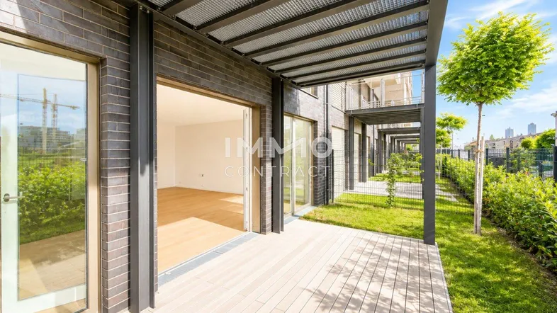 Moderne Terrasse mit Holzboden und Zugang zu einem hellen Innenraum, umgeben von Grünflächen.