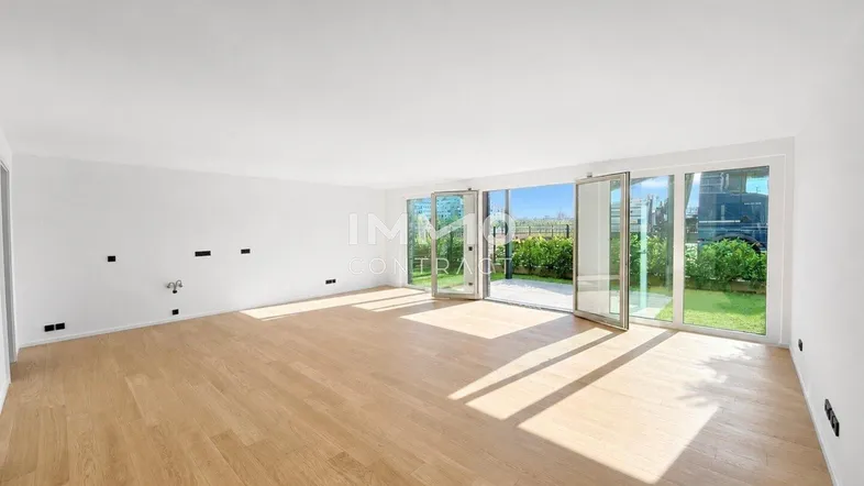 Helles, leeres Wohnzimmer mit Holzboden und großen Fenstern zum Garten.