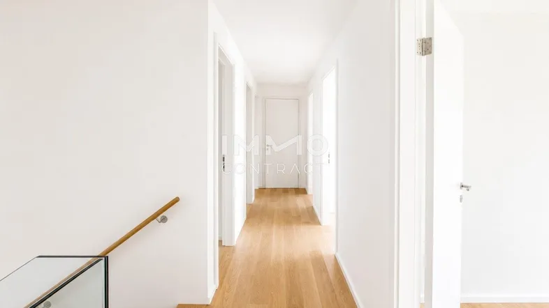 Heller Flur mit Holzfußboden und moderner Treppe mit Glasgeländer.