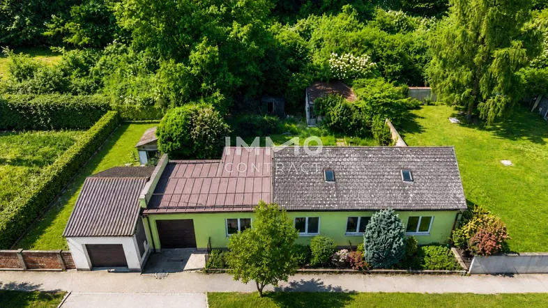 Vogelperspektive des grünen Hauses mit Garage, eingebettet in eine grüne Landschaft.